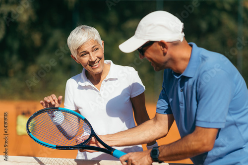 Tennis Coach Practicing Service with Senior Woman on Outdoor Tennis Class. © Microgen