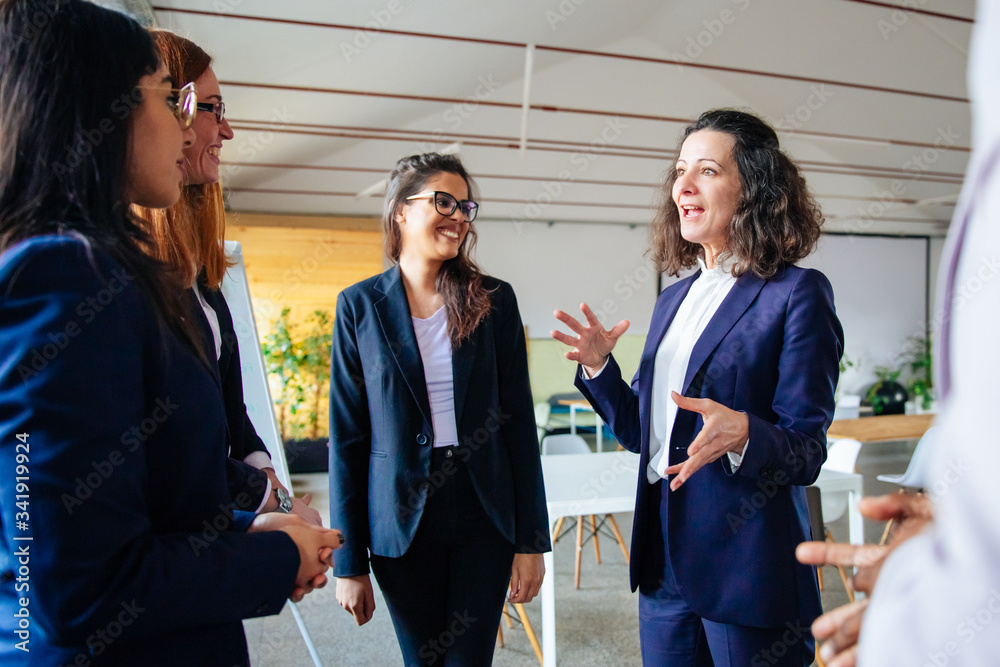 Smiling mature employee talking with younger colleagues. Cheerful office managers talking in office. Communication concept Smiling mature employee talking with younger colleagues. Cheerful office managers talking in office. Communication concept