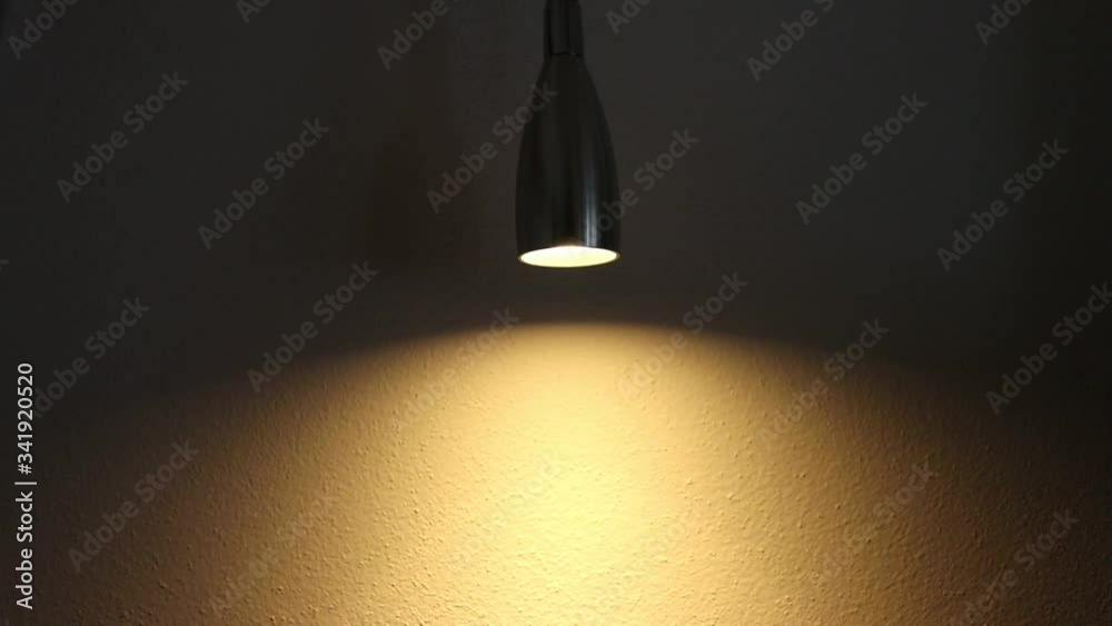 A dimmable light in a dark room and its effect on a wall. The brightness of the light increases and decreases. The dimmer is set on a small led light
