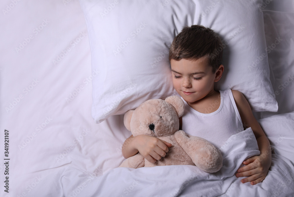 Little boy sleeping with teddy bear at home, top view. Bedtime