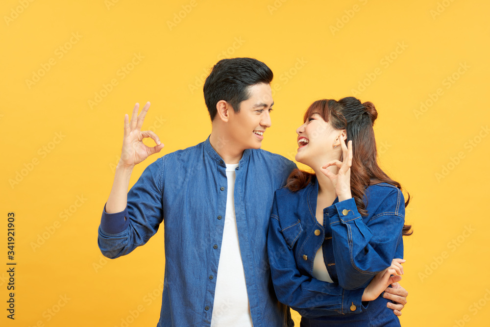 Young beautiful couple standing over isolated yellow background doing ok gesture with hand smiling, with happy face. Young beautiful couple standing over isolated yellow background doing ok gesture with hand smiling, with happy face.