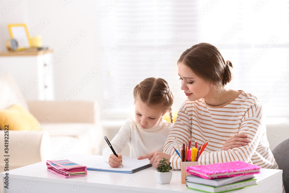 Woman helping her daughter with homework at table indoors Woman helping her daughter with homework at table indoors