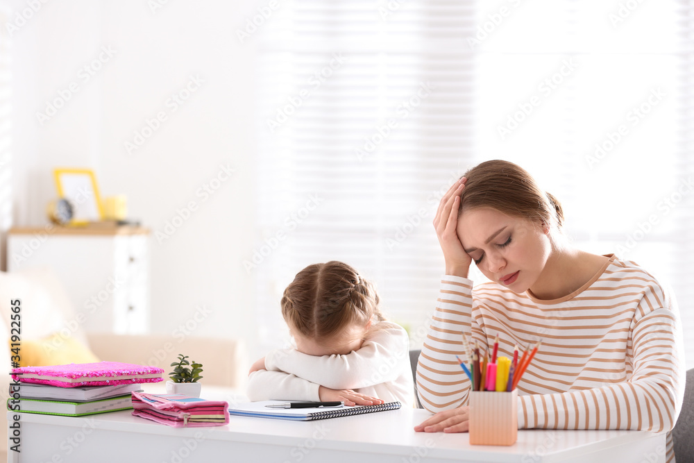 Upset mother and daughter doing homework together at table indoors