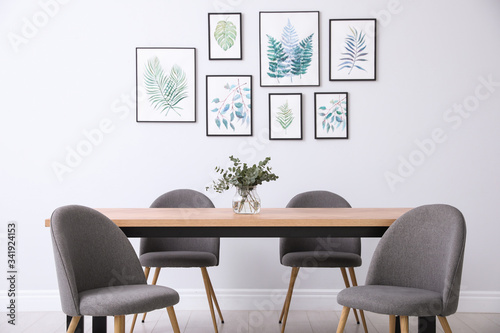 Stylish room interior with modern table  chairs and paintings of tropical leaves. Idea for design