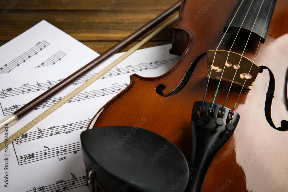 Fototapeta premium Beautiful violin, bow and note sheets on wooden table, closeup