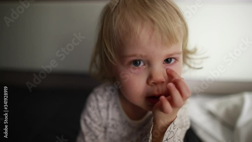 A small child with white hair looks at the camera and starts smiling