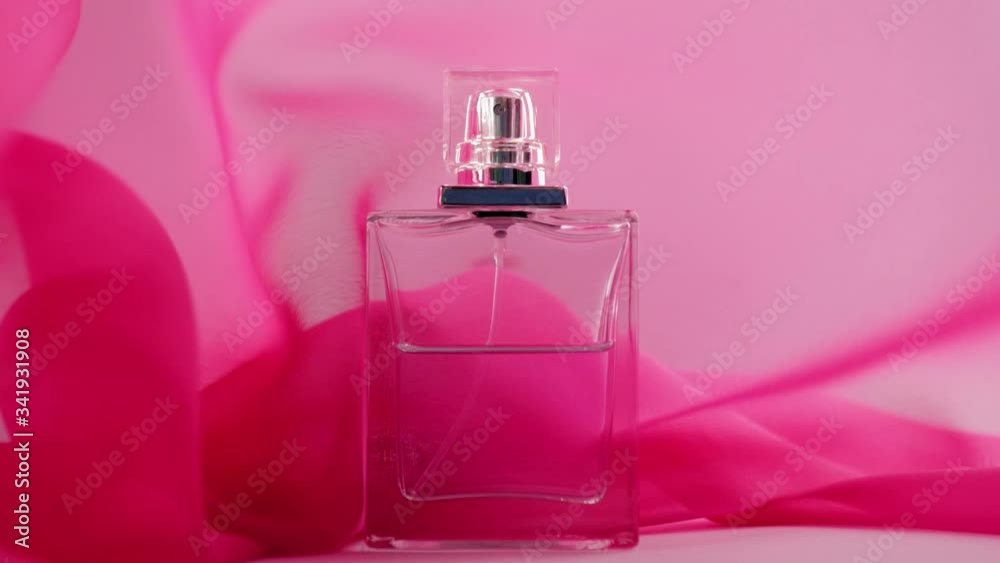 Flat surfaced perfume bottle with cyan perfumes or essential oils is on the table. Pink fabric flutters around and waves in the air around the perfume bottle. Concept of aroma and smell. Close up Flat surfaced perfume bottle with cyan perfumes or essential oils is on the table. Pink fabric flutters around and waves in the air around the perfume bottle. Concept of aroma and smell. Close up