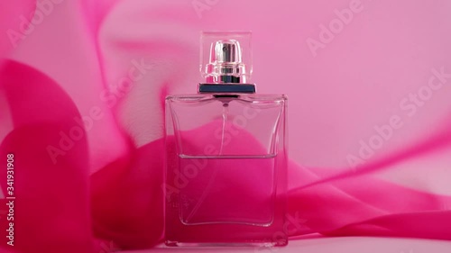 Flat surfaced perfume bottle with cyan perfumes or essential oils is on the table. Pink fabric flutters around and waves in the air around the perfume bottle. Concept of aroma and smell. Close up