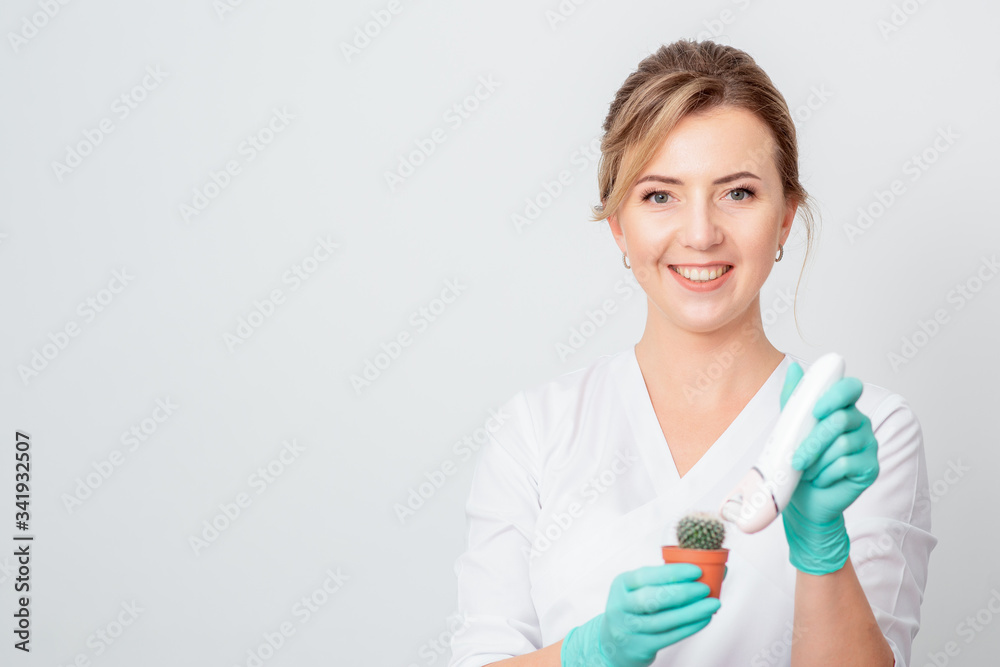 Cosmetologist is shaving green cactus in a brown pot with electric epilator wearing gloves smiling on white background. Concept of depilation, epilation and removal hair. Cosmetologist is shaving green cactus in a brown pot with electric epilator wearing gloves smiling on white background. Concept of depilation, epilation and removal hair.