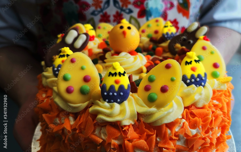 bright yellow and orange Easter cake with lots of sweets for decoration, two hands holding the cake