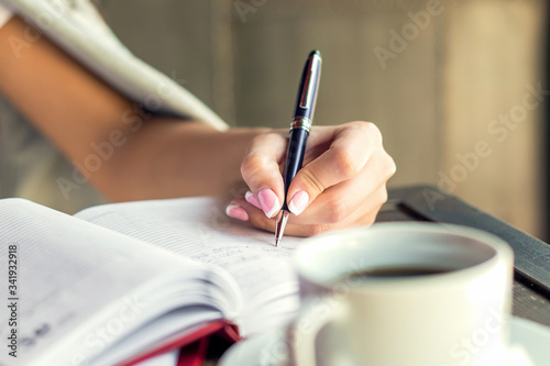 Business woman hand is writing in notepad with pen at cafe.