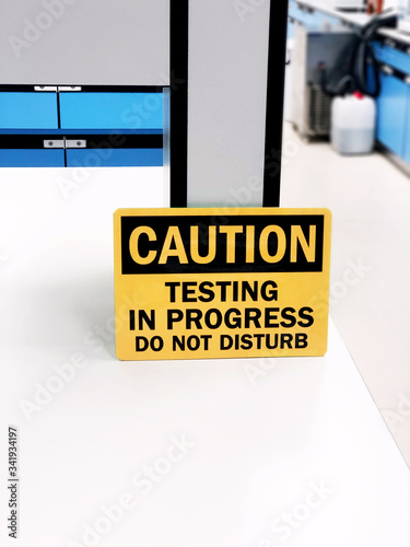 Caution testing in progress do not disturb, a safety sign warning on bench laboratory, useful for caution who working in the Lab room. Think Safety first concept.