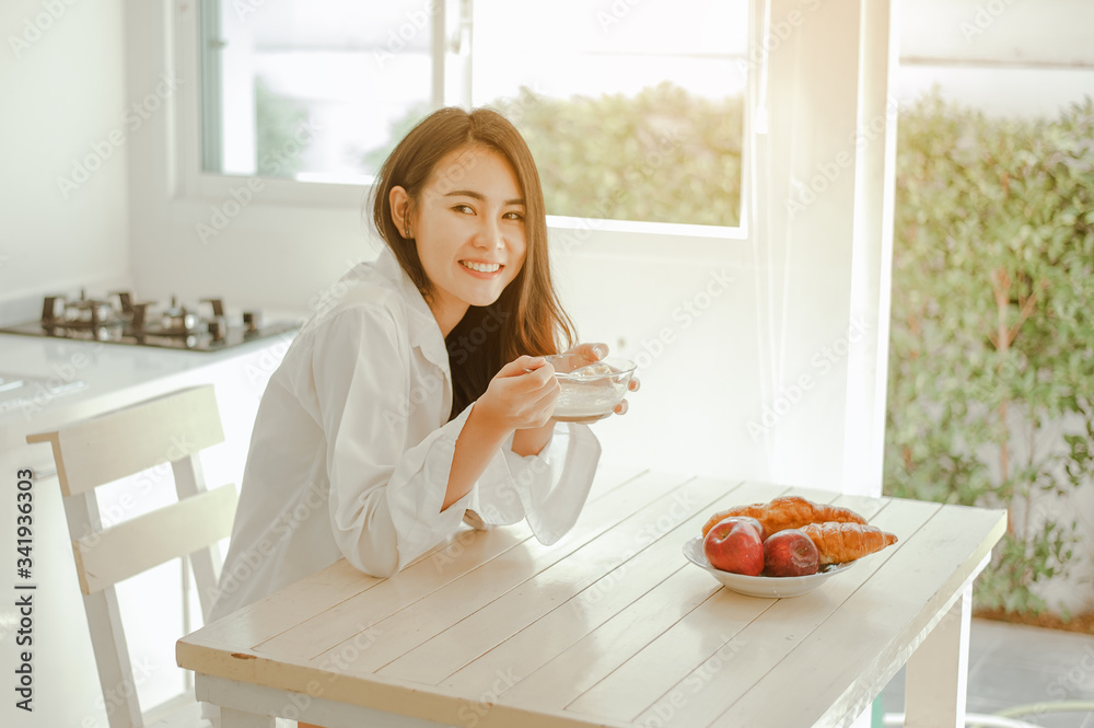 Young woman asia wake up refreshed in the morning and relaxing eat coffee, cornflakes, bread and apple for breakfast at house on holiday. Asian, asia, relax, breakfast, refresh, lifestyle concept.