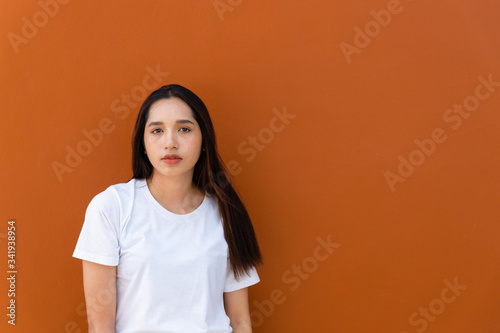 Portrait of beautiful Asian young woman with her black hair wearing a white T-shirt. Close up on her charming face with a brown background and copy spaces