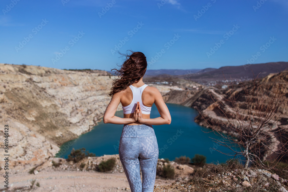 Young pretty woman is practicing yoga at mountain lake in shape of heart.
