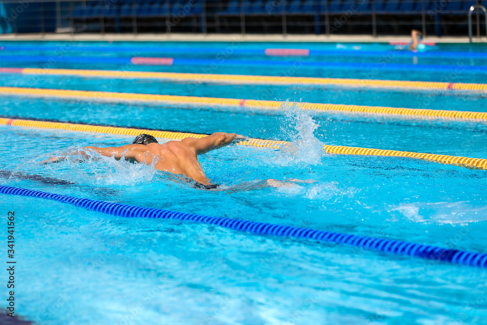 Athletic man swimming in butterfly style in the swimming pool with clear blue water.