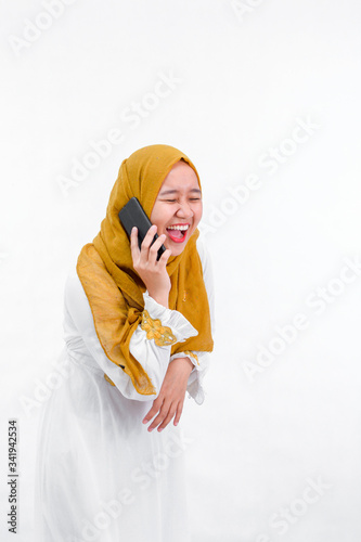 portrait of attractive asian muslim woman on white dress with hijab using a smartphone and laugh while have a call isolated over white background