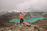 Kyrgyzstan. Karakol. Alakel. A beautiful alpine lake of turquoise color among high snow-capped mountains. A girl in a bright jacket and sportswear looks into the distance. Trekking. Trekking Stormy
