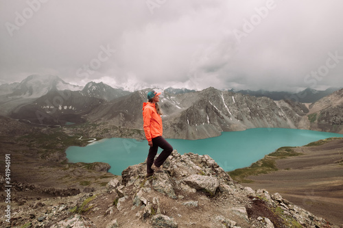 Kyrgyzstan. Karakol. Alakel. A beautiful alpine lake of turquoise color among high snow-capped mountains. A girl in a bright jacket and sportswear looks into the distance. Trekking. Trekking Stormy