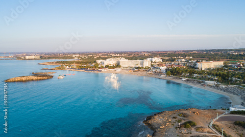 Aerial bird's eye view of famous Nissi beach coastline, Ayia Napa, Famagusta, Cyprus.Landmark tourist attraction islet bay at sunrise with golden sand, sunbeds, sea restaurants in Agia Napa from above © f8grapher