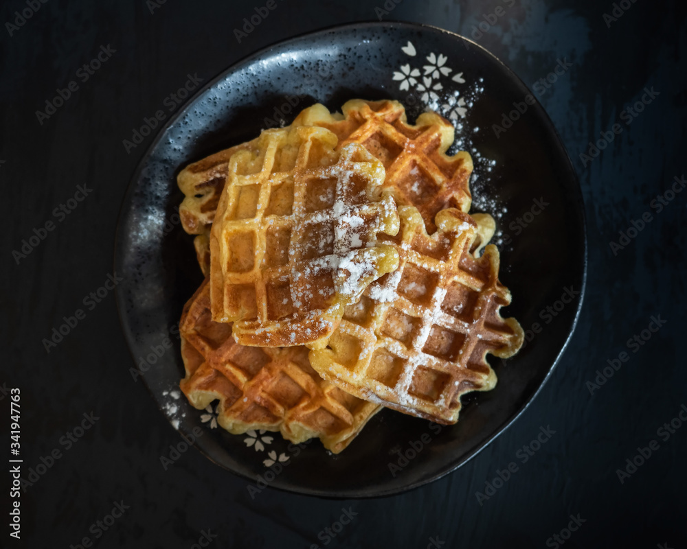 Homemade waffles with icing sugar in a deep black vase on a black table Homemade waffles with icing sugar in a deep black vase on a black table