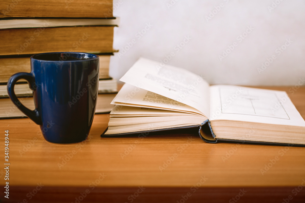 an expanded book, a blue cup and a stack of books on a table with a white background with place for text an expanded book, a blue cup and a stack of books on a table with a white background with place for text