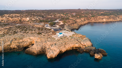 Aerial bird’s eye view of coastline sunset, landmark white washed chapel Agioi Anargyroi, Cavo Greco Protaras, Famagusta, Cyprus from above. Ayioi Anargiroi church, rock cliff sea caves at sunrise. photo