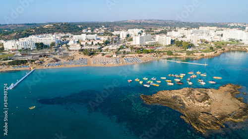 Fototapeta Naklejka Na Ścianę i Meble -  Aerial bird's eye view of Fig tree bay in Protaras, Paralimni, Famagusta, Cyprus. Tourist attraction golden sandy beach with boats, sunbeds, sea restaurants, water sports on summer holidays from above