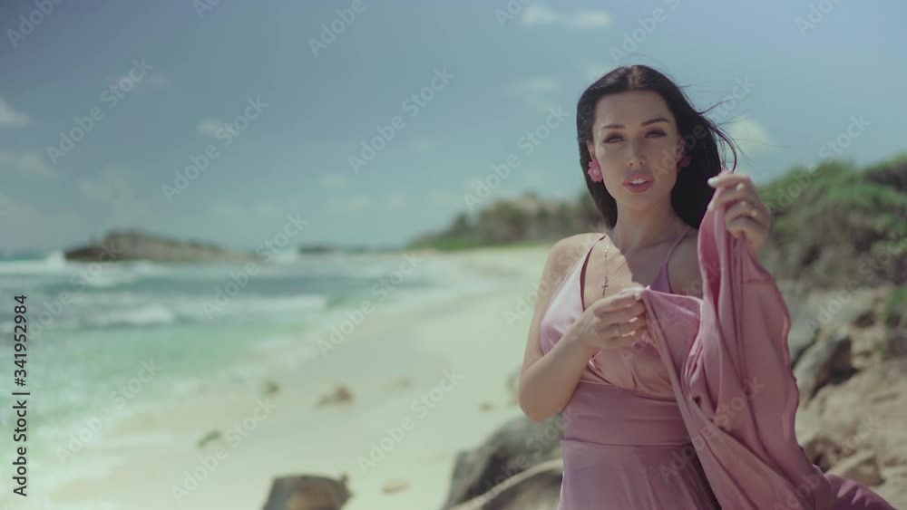 Beautiful fashionable woman in a pink dress posing in front of the camera on the seashore. Beautiful fashionable woman in a pink dress posing in front of the camera on the seashore.