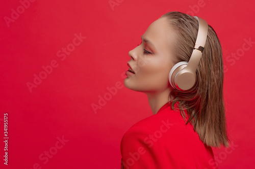 A beautiful young girl in a red jacket and wireless headphones listens to the song with a good mood. Music poster.