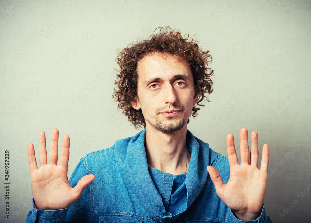 Curly young man gesture stop. On a gray background Curly young man gesture stop. On a gray background