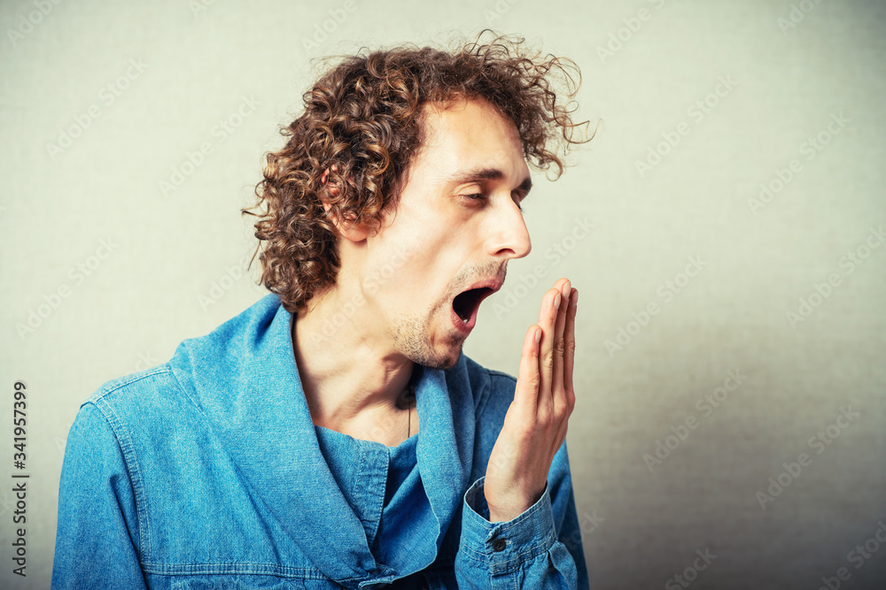 The curly-haired man yawning gesture. On a gray background. The curly-haired man yawning gesture. On a gray background.
