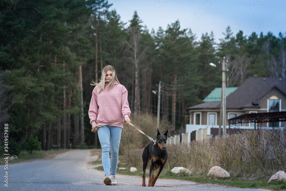 A girl in jeans walks with a Doberman in a holiday village.