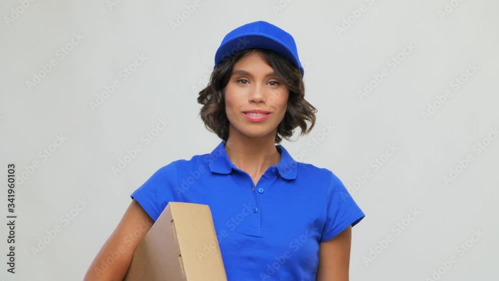 mail service and shipment concept - happy smiling delivery girl with parcel box in blue uniform over grey background mail service and shipment concept - happy smiling delivery girl with parcel box in blue uniform over grey background