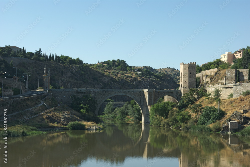 A view of the Alcantara bridge at Toledo, Spain.  The elegant shape of the bridge is reflected on the still waters of the river Tagus