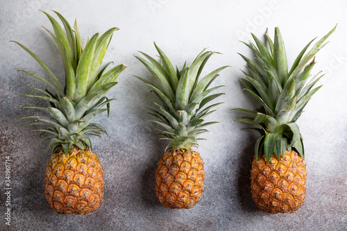 Three whole fresh ripe pineapples on concrete background. Food background. Top view, copy space.