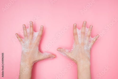 Feminime hands with soapy bubbly foam on pink background,
