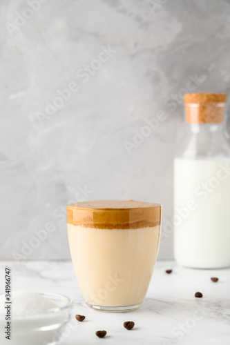 Korean coffee drink. Iced Dalgona coffee in glass cup on light table. Trendy refreshment creamy whipped coffee. Vertical orientation, copy space. Gray concrete background