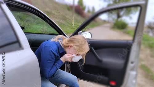 The blonde girl became ill from driving a car. Vomiting forced her to look out of the car so that the vomit would not enter the passenger compartment. The girl suffers from kinetosis, motion sickness. photo