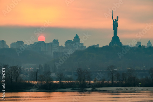 View from the left bank at sunset over the Dnieper River, the Motherland Monument and the right-bank part of Kyiv. photo