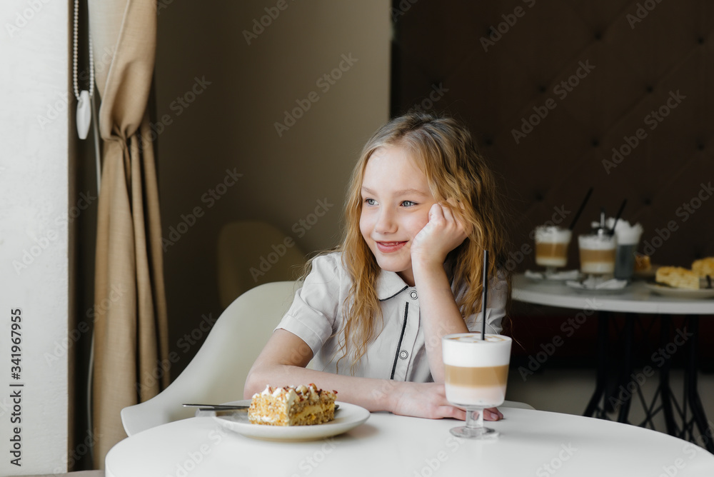 A cute little girl is sitting in a cafe and looking at a cake and cocoa close-up. Diet and proper nutrition A cute little girl is sitting in a cafe and looking at a cake and cocoa close-up. Diet and proper nutrition