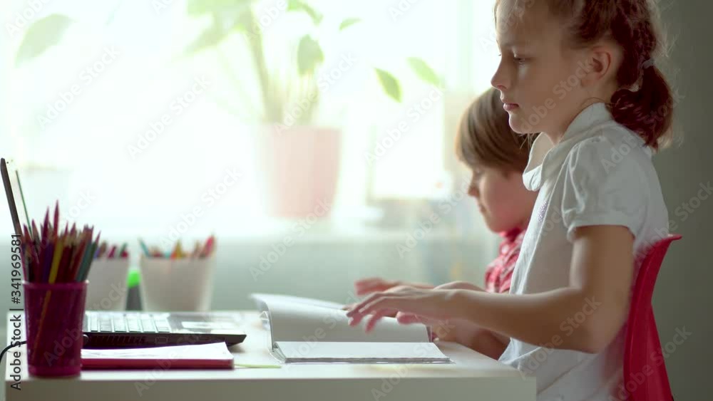 Online distance learning at home during the worldwide coronavirus epidemic covid19. Brother and sister use a laptop. Charming kids do their homework. Home education concept. Online distance learning at home during the worldwide coronavirus epidemic covid19. Brother and sister use a laptop. Charming kids do their homework. Home education concept.