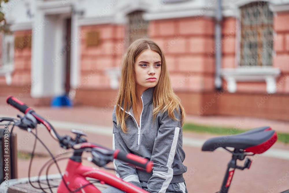 A woman is resting from cycling on a city bench.