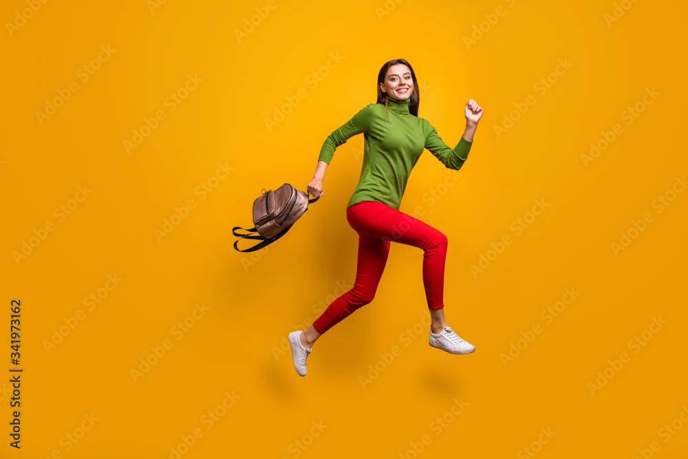Full body profile photo of funky pretty lady jumping high holding cool youngster bag rushing home after studying wear casual green jumper red pants isolated yellow color background
