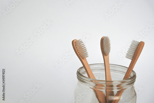 three bamboo tooth brushes in a glass jar on a white background  copy space