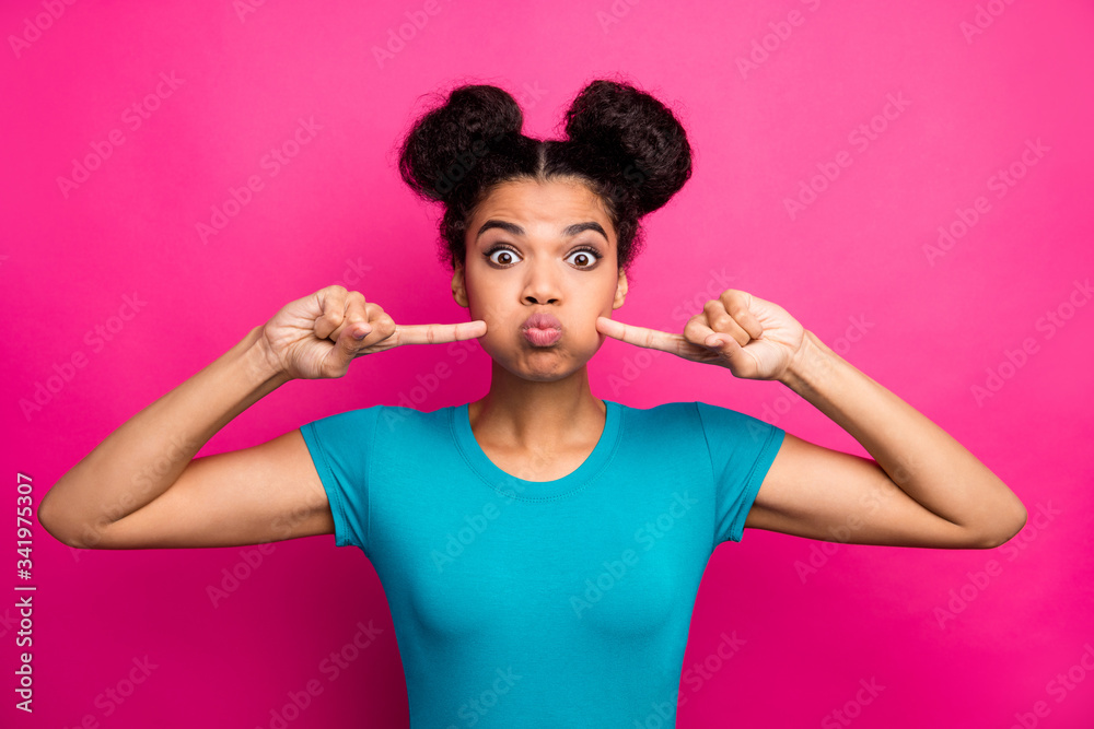 Closeup photo of crazy funky dark skin lady two buns hold breath press fingers cheekbones funny facial expression wear blue casual t-shirt isolated magenta color background
