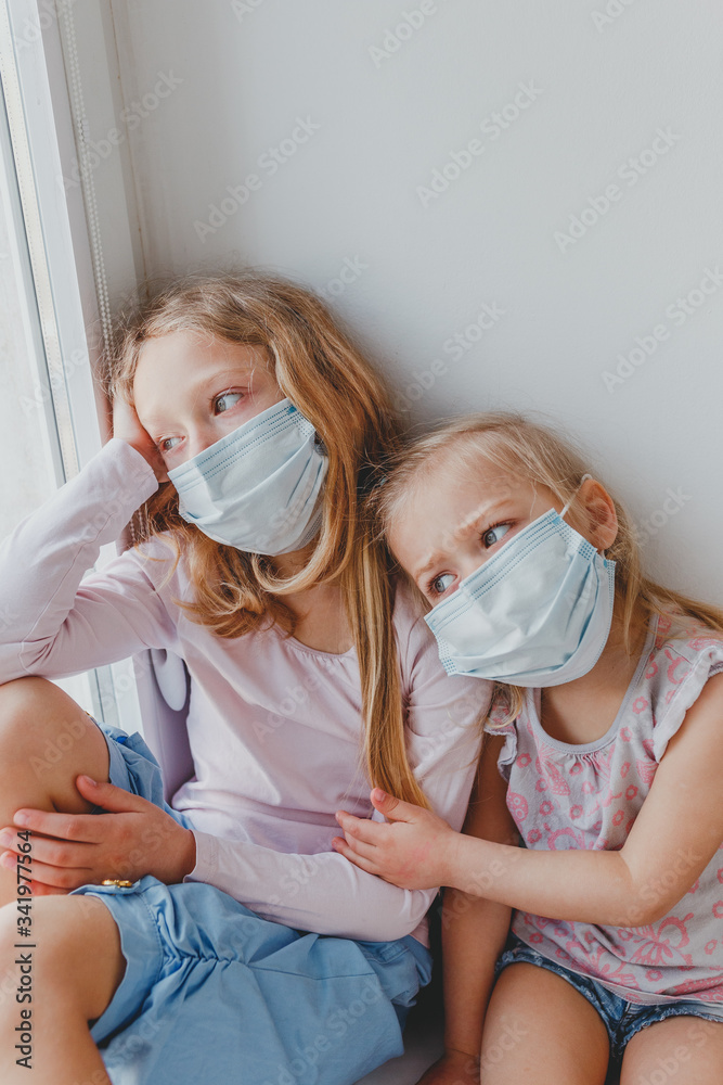 small children in masks from coronavirus remained at home and look out the window. children are sad covid