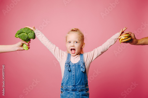 Hungry girl is hard to choose a burger or broccoli on pink background. Unheathy vs healthy food. Concept of choice. photo