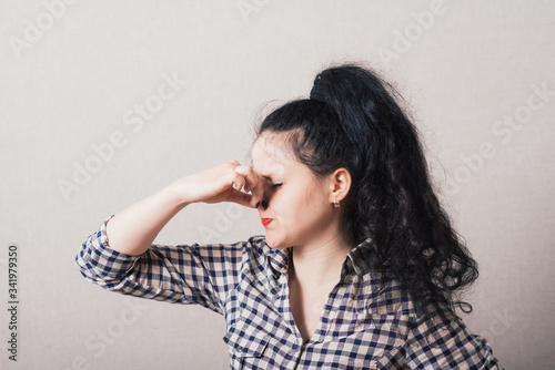 woman covering her eyes, hand covering her nose. On a gray background.