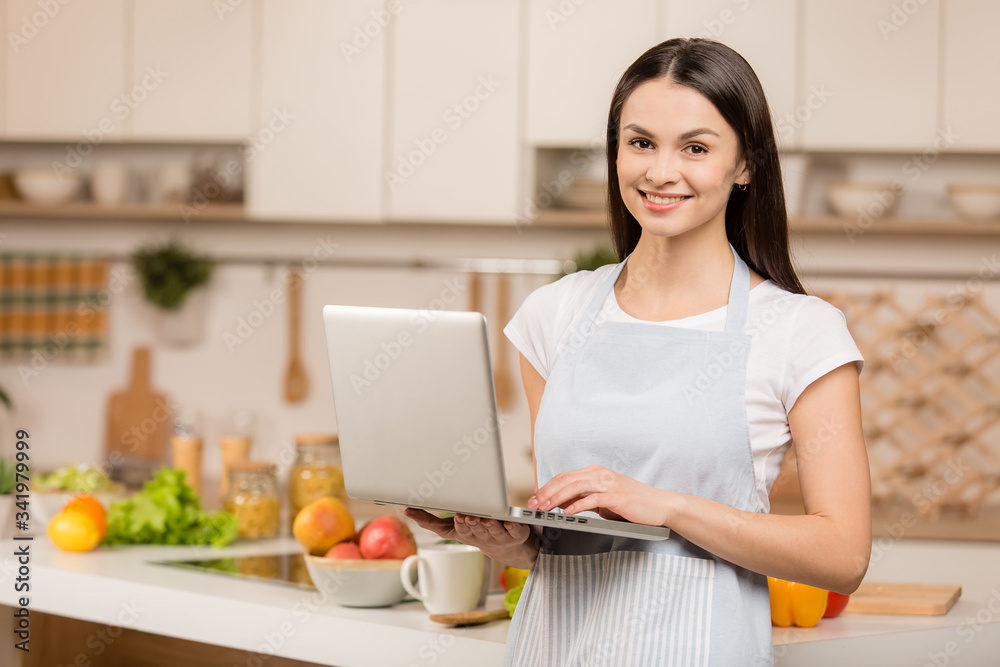 Young Woman in kitchen with laptop computer looking recipes, smiling. Food blogger concept Young Woman in kitchen with laptop computer looking recipes, smiling. Food blogger concept